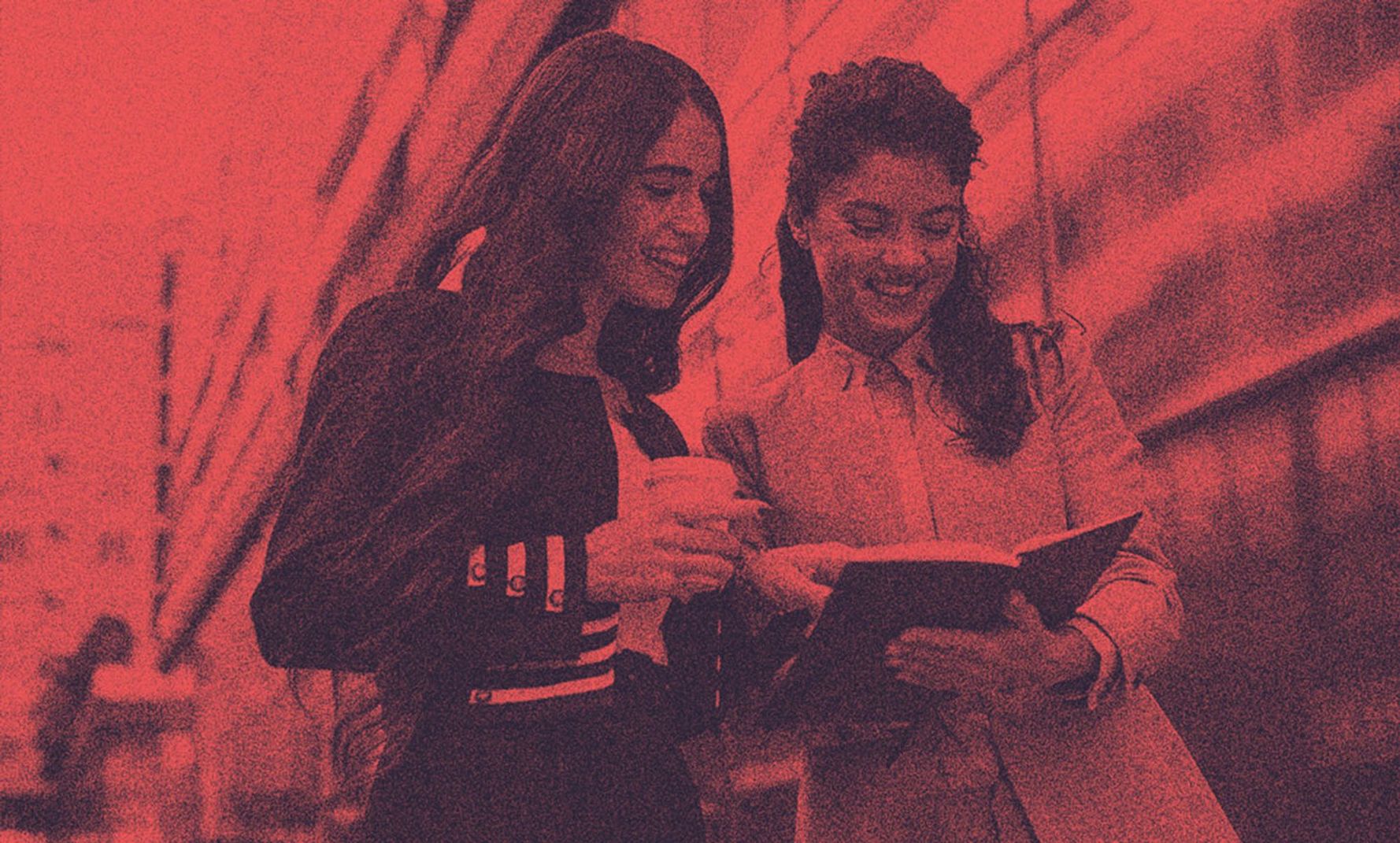 Two women talking looking inside a book.