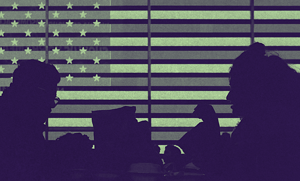 A group of people walking beside a screen on which the American flag is projected.
