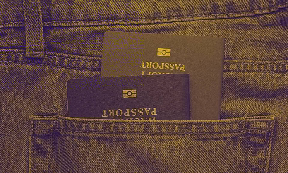 Two passports are seen stacked inside a back pocket of a person's jeans.