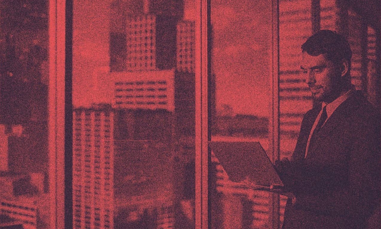 A man in suit standing, holding his laptop.