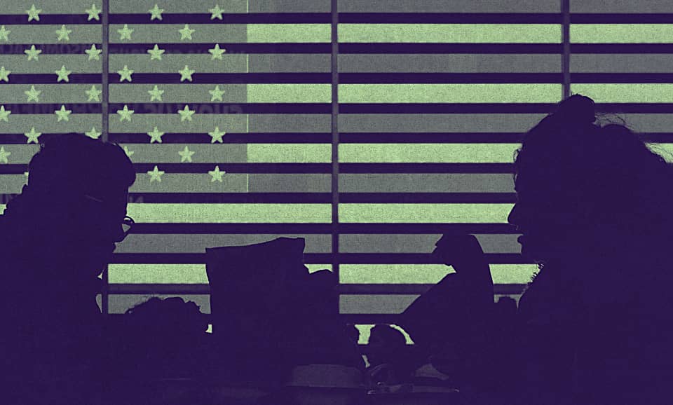 A group of people walking beside a screen on which the American flag is projected.