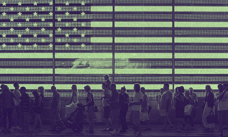a group of people walking beside a screen with the U.S. flag projected on.