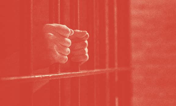 A person's hands are shown holding prison bars.