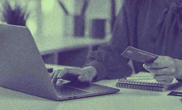 Bir insan elinde kredi kartıyla laptop ekranına bakmakta.