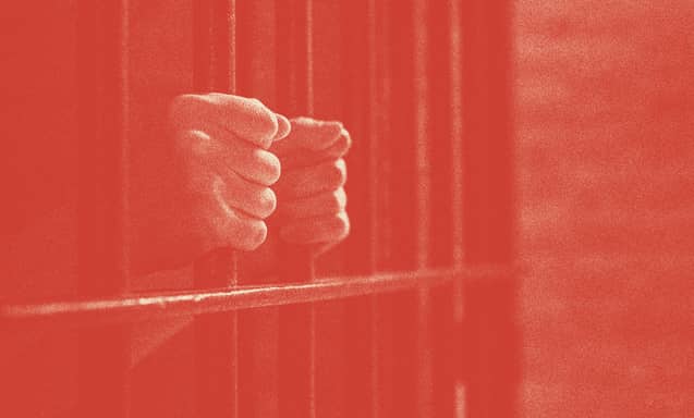 A person's hands are shown holding prison bars.