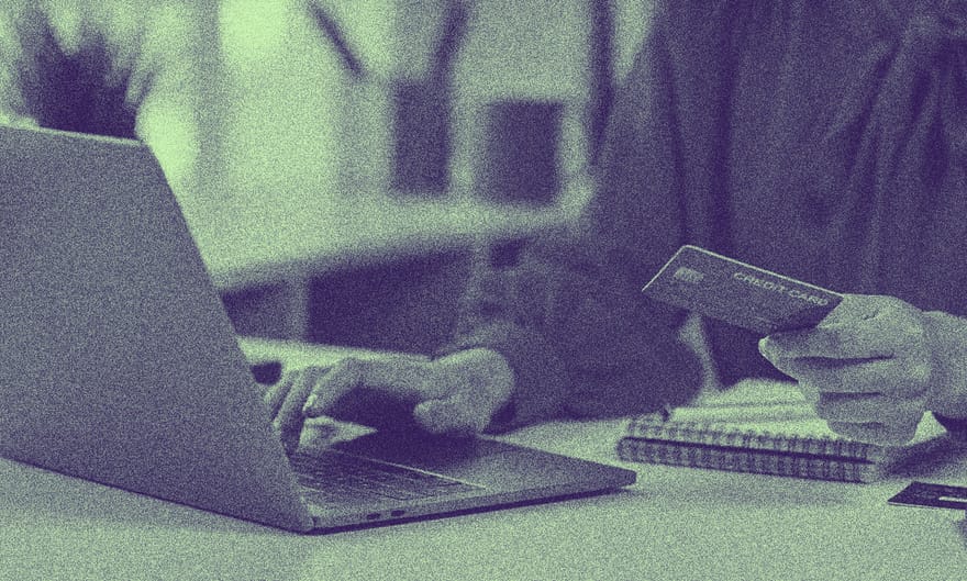 Bir insan elinde kredi kartıyla laptop ekranına bakmakta.