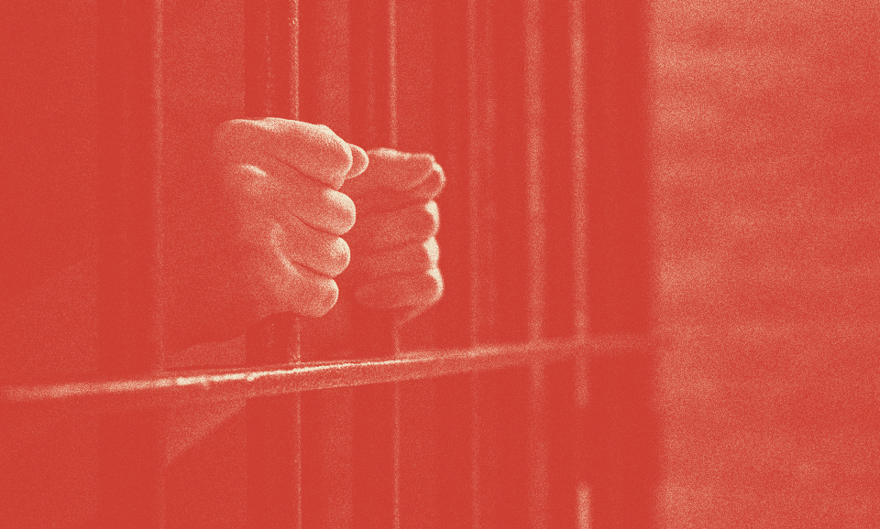 A person's hands are shown holding prison bars.